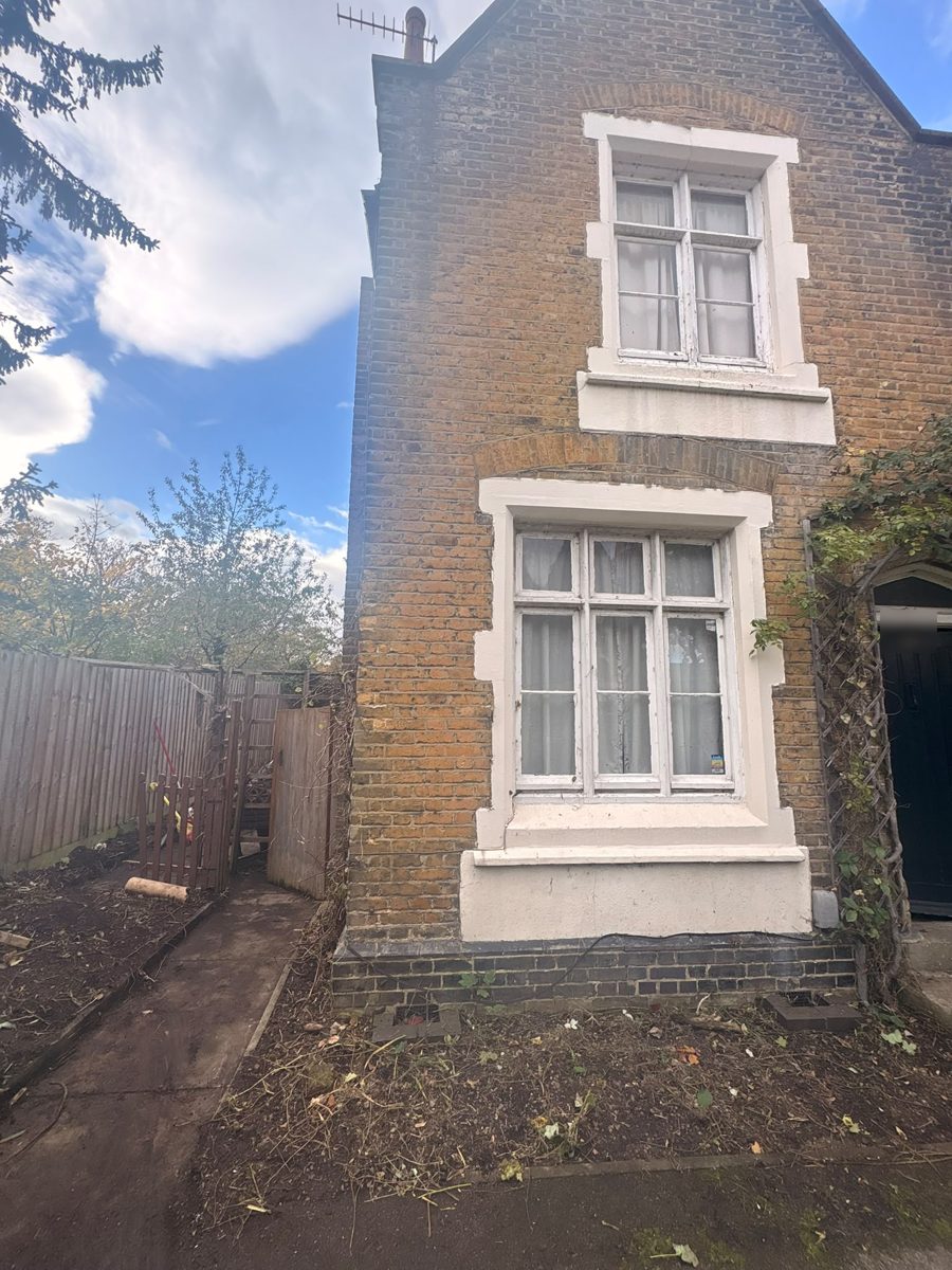 Front and side of a brick house in Ware with the beds cleared to bare soil and a clear path leading to the side gate