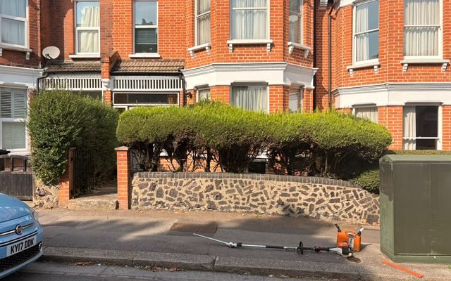 Front garden hedge in St Albans with a long-reach hedge trimmer and fuel can set down on the pavement